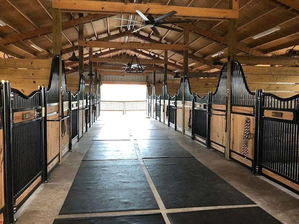 A horse barn aisle featuring black metal stall doors and wood-paneled walls — 7565 Polo Square, Vero Beach FL 32968, VERO BEACH, FL