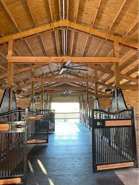 A view down the center aisle of a horse barn with metal stall doors — 7565 Polo Square, Vero Beach FL 32968, VERO BEACH, FL