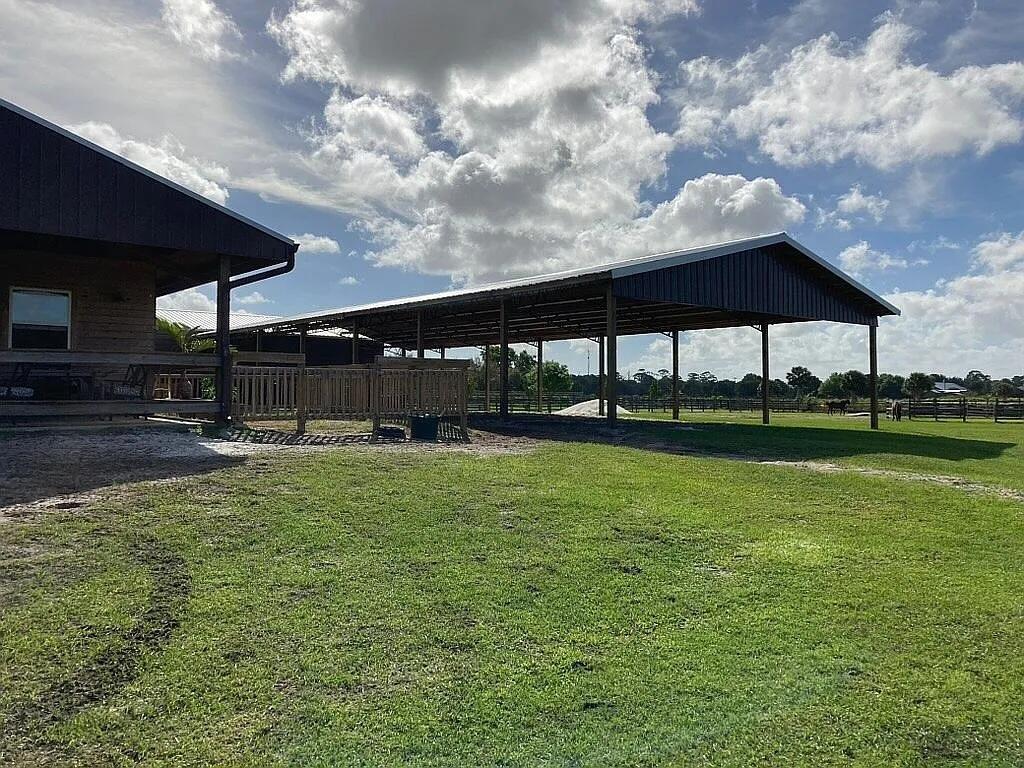 A large open-sided metal barn structure stands next to a house on a grassy lot — 7565 Polo Square, Vero Beach FL 32968, VERO BEACH, FL