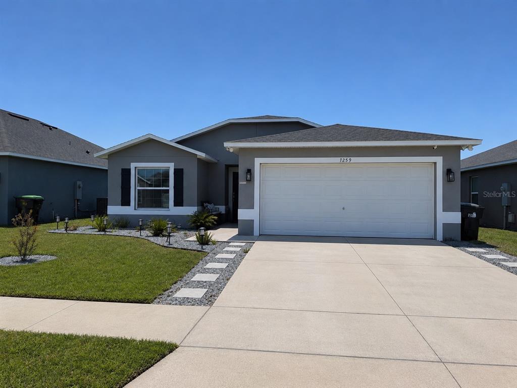 The exterior rear view of a gray stucco house features a covered patio and lawn — 7259 HOLLY CREEK ROAD, MOUNT DORA, FL