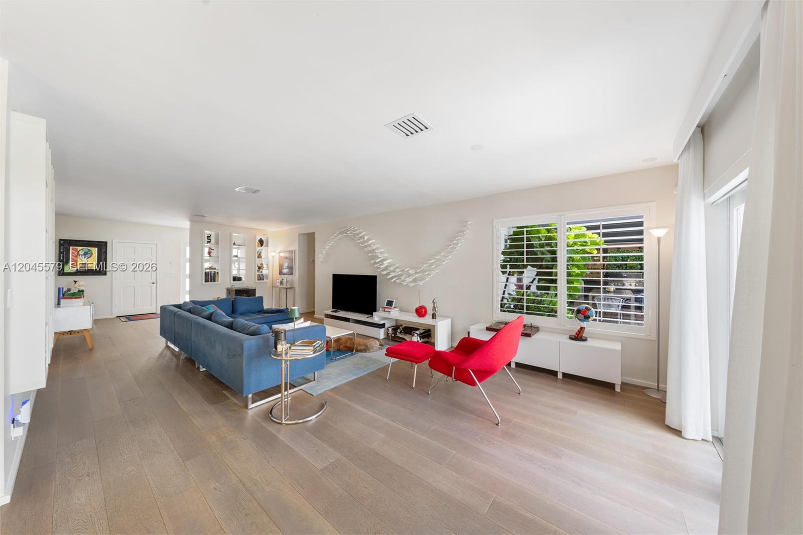 A living room features a blue sectional sofa, a red chair, and light wood flooring — 12944 Banyan Rd, North Miami FL 33181, NORTH MIAMI, FL