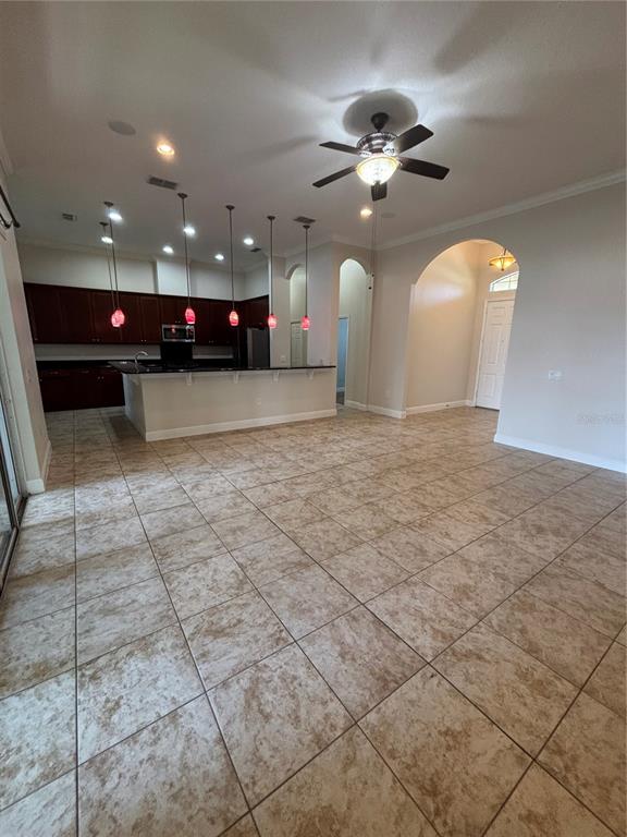 An open-concept kitchen with dark cabinets and a breakfast bar overlooks a tiled living area — 3650 PEACE PIPE WAY, CLERMONT, FL