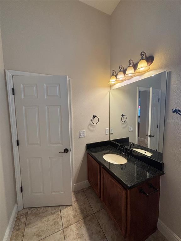 A bathroom vanity features a dark granite countertop, wooden cabinetry, and a wall-mounted mirror — 3650 PEACE PIPE WAY, CLERMONT, FL