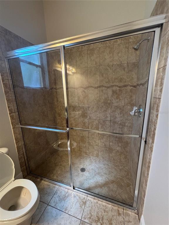 A tiled walk-in shower with a glass sliding door is located next to a toilet — 3650 PEACE PIPE WAY, CLERMONT, FL