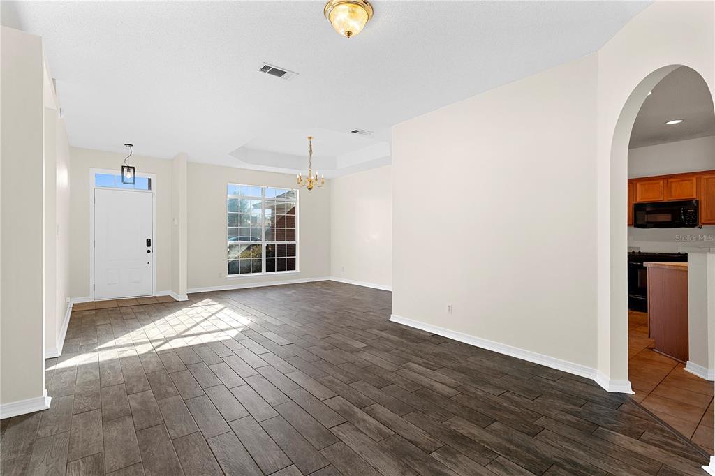 A living room with wood-look tile flooring, a tray ceiling, and an arched kitchen entryway — 6622 HALLENDALE DRIVE, PENSACOLA, FL