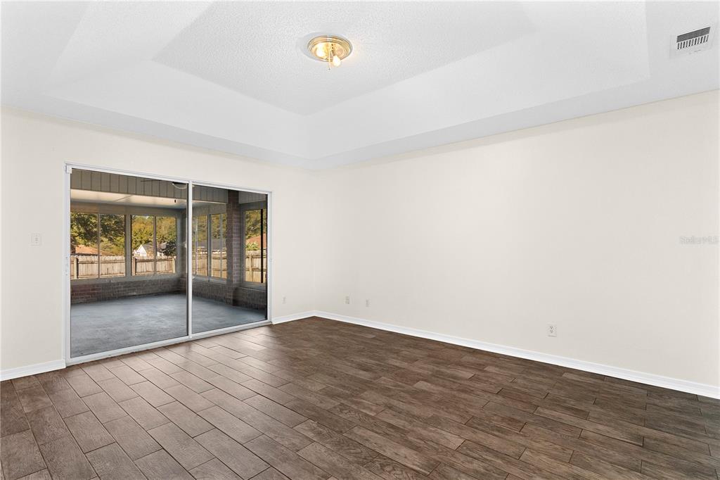 An empty room with a tray ceiling, wood-look tile floors, and sliding glass doors — 6622 HALLENDALE DRIVE, PENSACOLA, FL