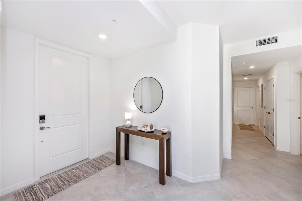 A bright entryway features a white door, a dark wood console table, and tile flooring — 17640 BORACAY COURT UNIT 102, VENICE, FL