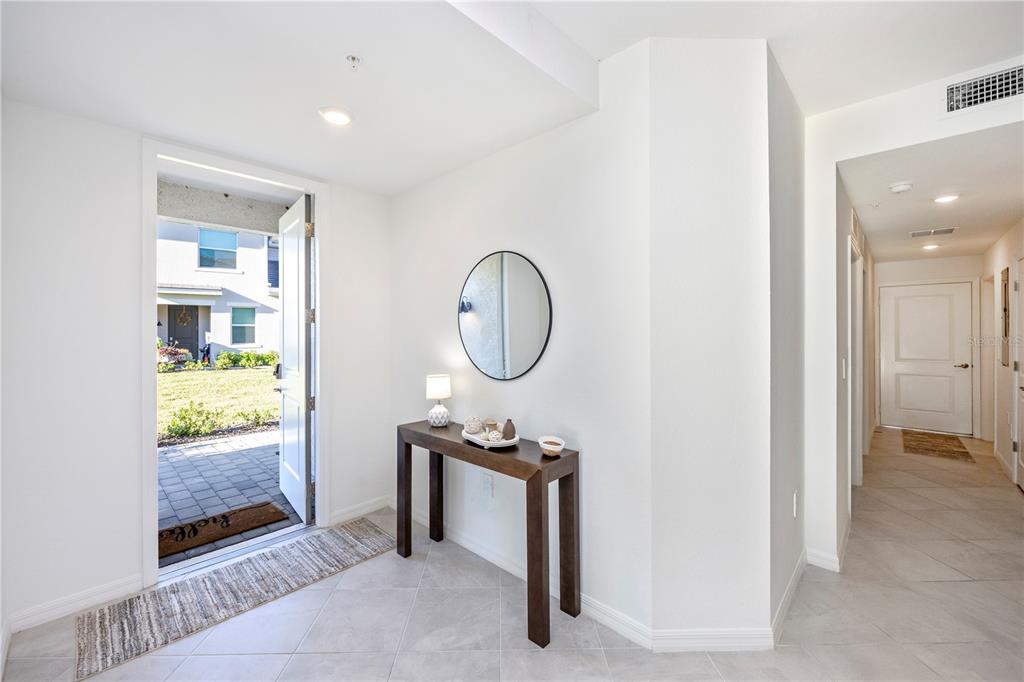 A bright entryway features white walls, tile flooring, a console table, and an open front door — 17640 BORACAY COURT UNIT 102, VENICE, FL