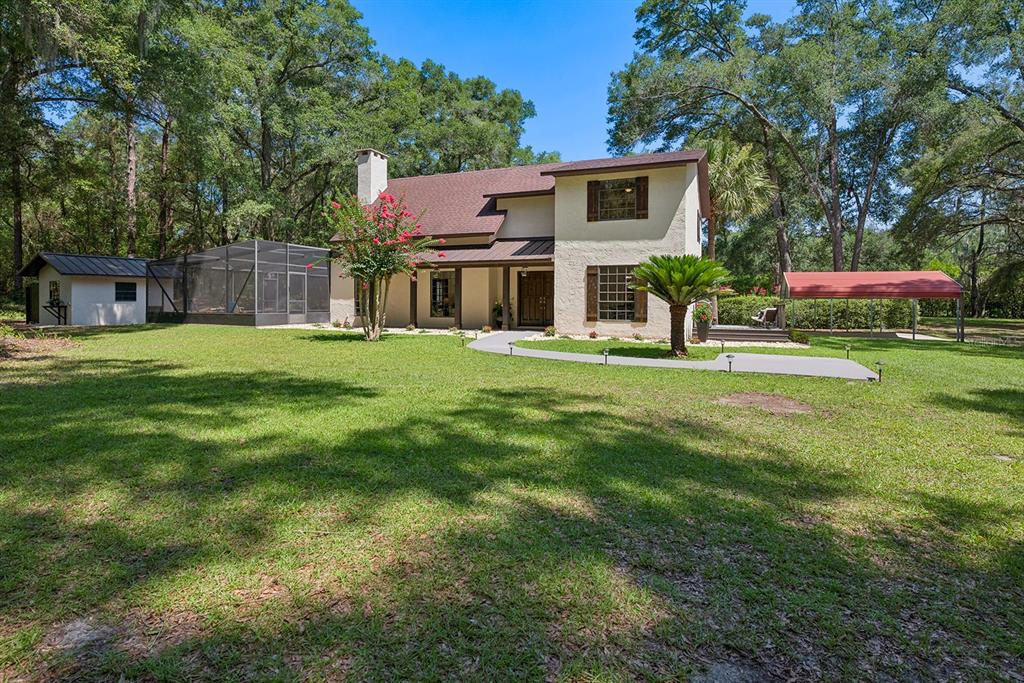 A two-story house with a screened-in patio, a metal carport, and a large grassy yard — 22110 SW 15TH AVENUE, NEWBERRY, FL