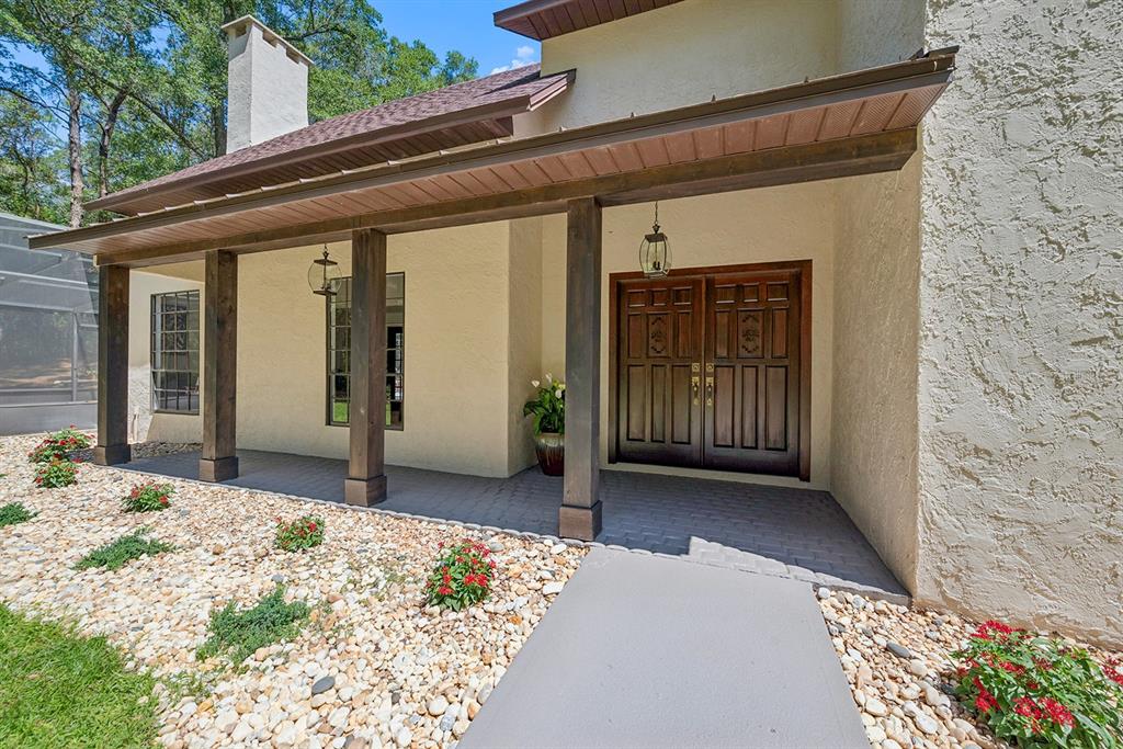 A front porch with wooden pillars leads to double wooden doors on a stucco house — 22110 SW 15TH AVENUE, NEWBERRY, FL