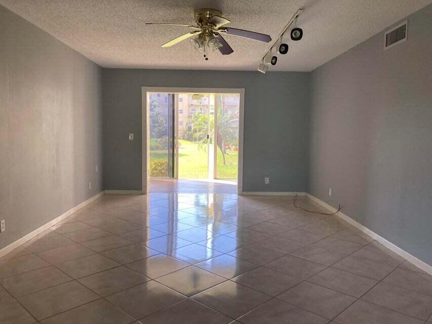 An empty living room with light blue walls, tile flooring, a ceiling fan, and sliding doors — 300 NE 26th Avenue NE # 1040, Boynton Beach FL 33435, BOYNTON BEACH, FL