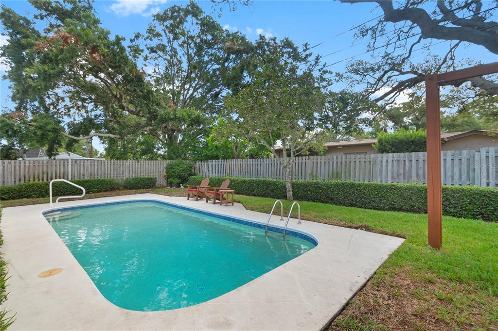 A backyard features a rectangular swimming pool with a concrete deck and a wooden fence — 1707 RIDGEWAY DRIVE, CLEARWATER, FL