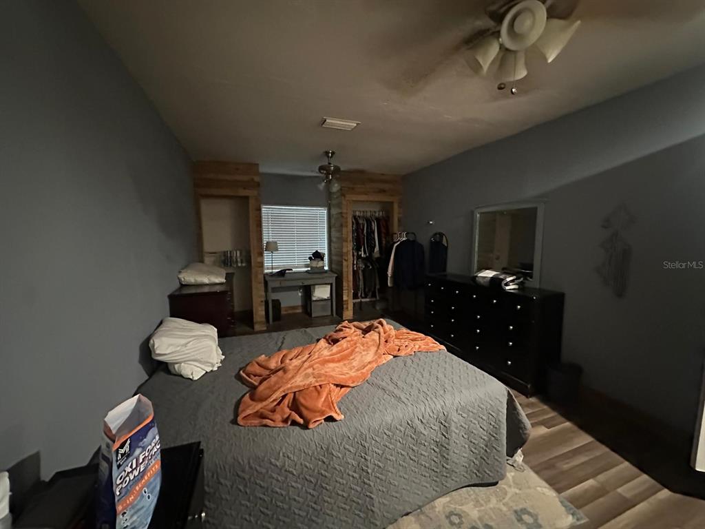 A bedroom features a bed with a gray quilt, dark furniture, and two open closets — 10040 62ND STREET N, PINELLAS PARK, FL