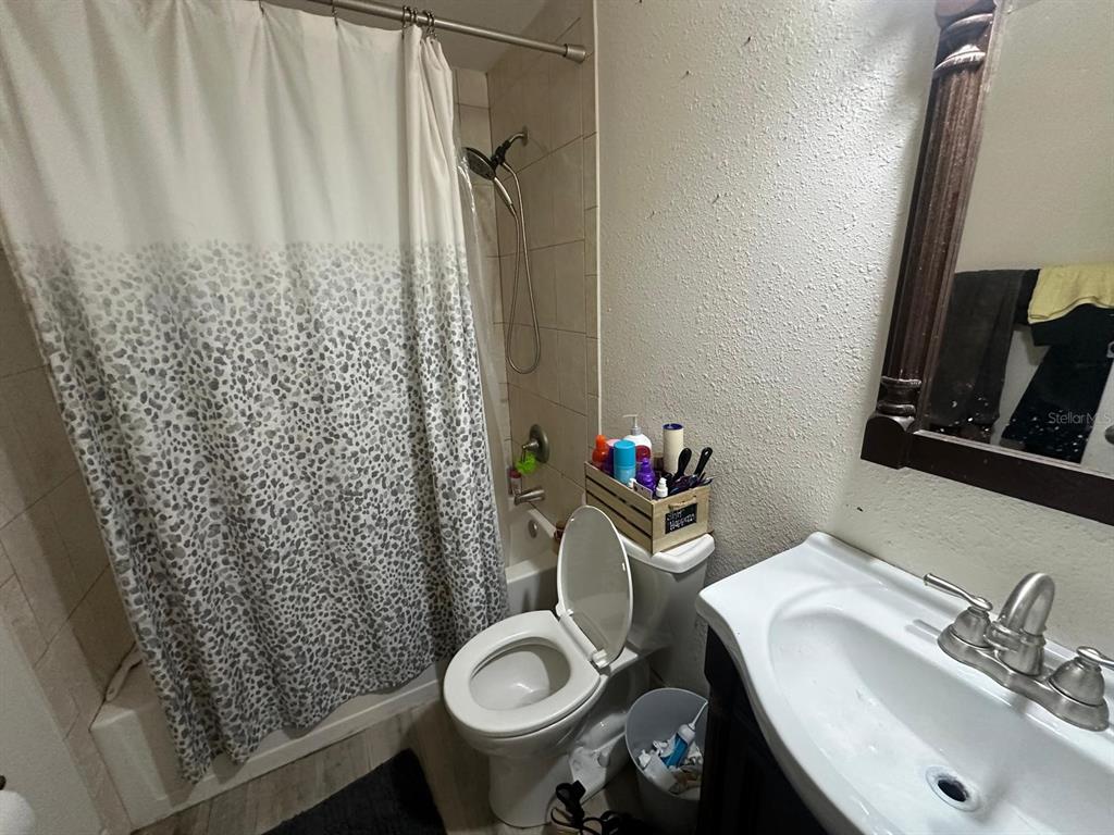 A bathroom features a shower with a patterned curtain, a toilet, and a vanity sink — 10040 62ND STREET N, PINELLAS PARK, FL
