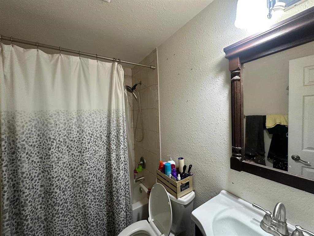 A bathroom features a shower with a patterned curtain, a toilet, and a wooden vanity mirror — 10040 62ND STREET N, PINELLAS PARK, FL