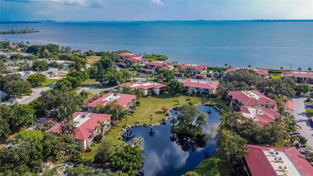 An aerial view of a waterfront apartment complex featuring red roofs and a central pond — 3415 WILD OAK BAY BOULEVARD UNIT 427, BRADENTON, FL