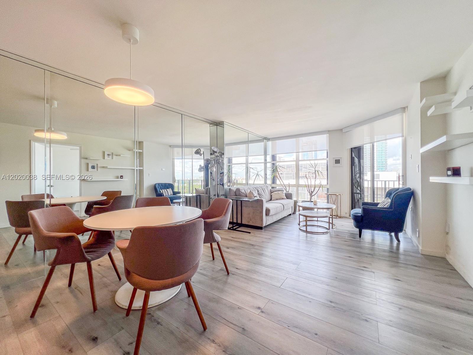 A living and dining area features light wood floors, mirrored walls, and a balcony view — 1901 Brickell Ave # B2004, Miami FL 33129, MIAMI, FL