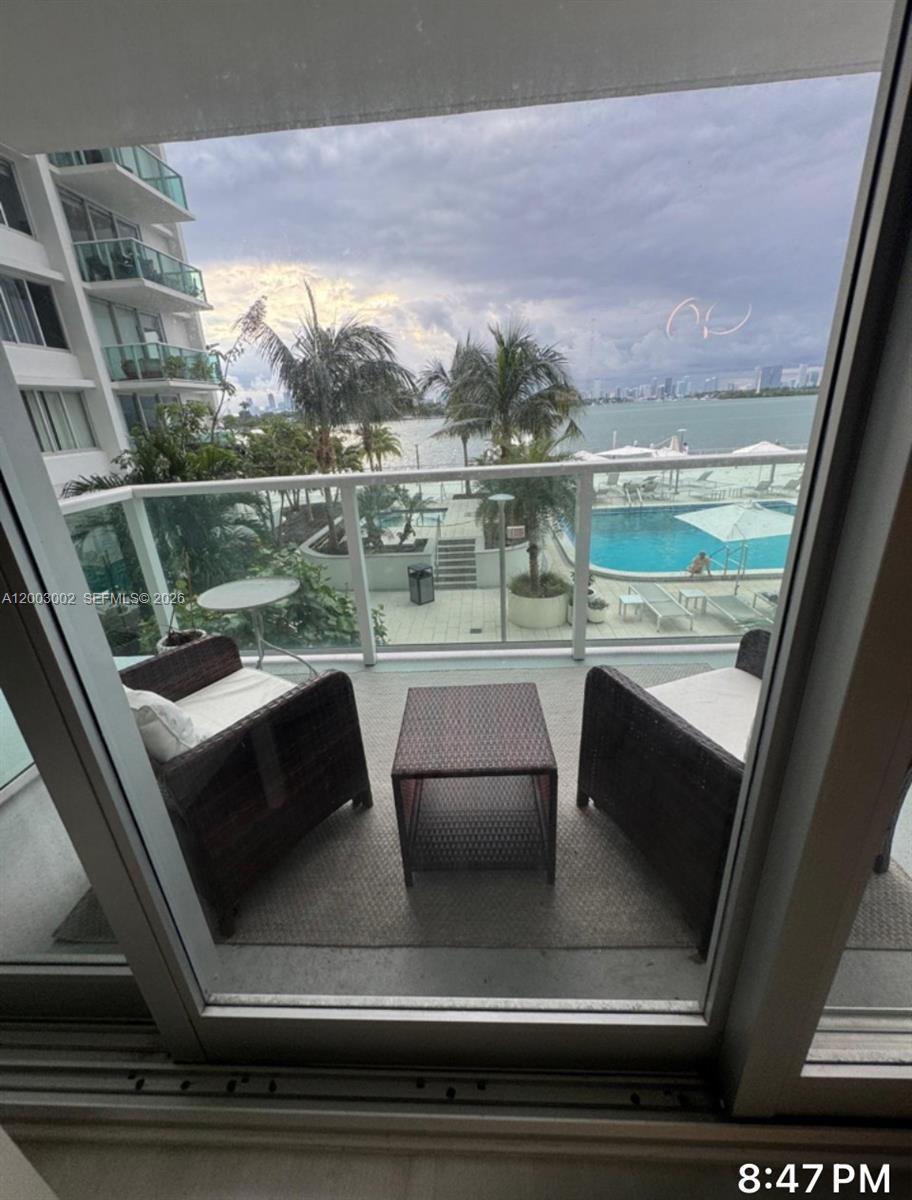 A balcony with two wicker chairs and a small table overlooks a swimming pool — 1000 West Ave # 218, Miami Beach FL 33139, MIAMI BEACH, FL