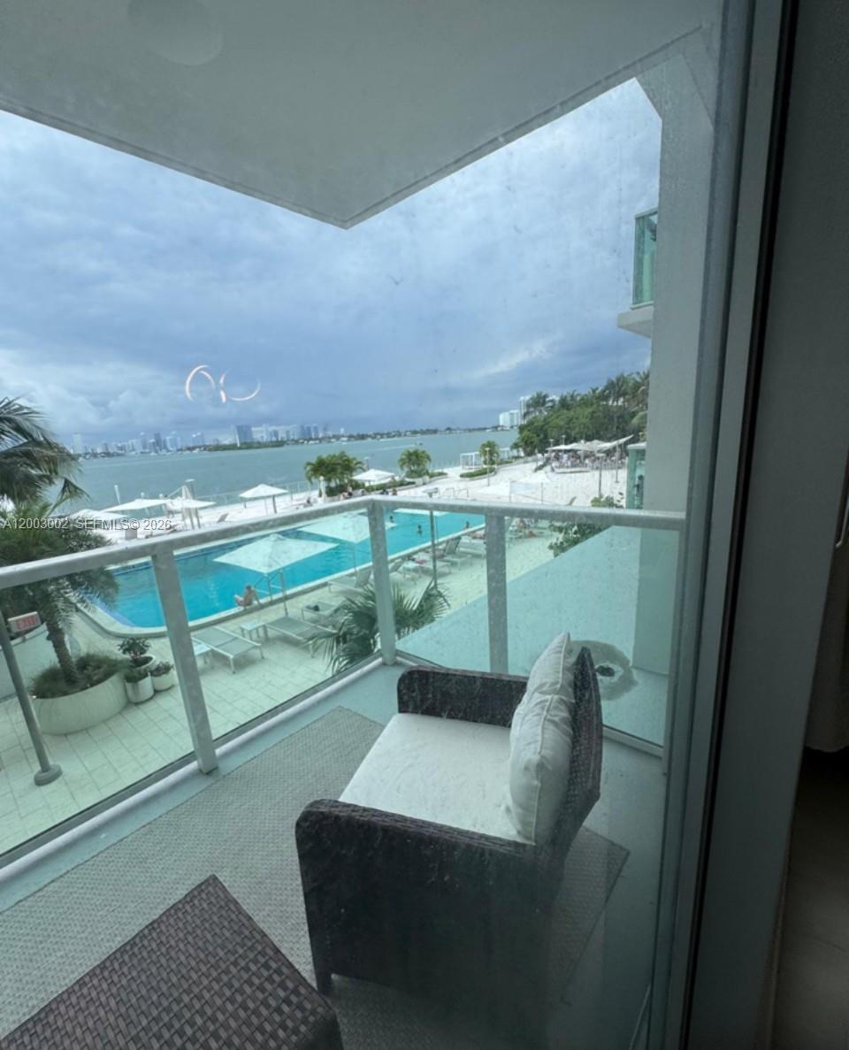 A balcony with a chair overlooks a swimming pool, sandy beach, and a bay — 1000 West Ave # 218, Miami Beach FL 33139, MIAMI BEACH, FL