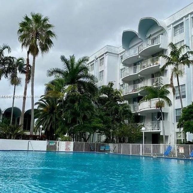 A swimming pool sits in front of a multi-story white apartment building with balconies — 492 NW 165th St Rd # 415, Miami FL 33169, MIAMI, FL
