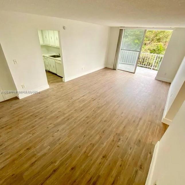 An empty living room with light wood-look flooring leads to a kitchen and a balcony — 492 NW 165th St Rd # 415, Miami FL 33169, MIAMI, FL