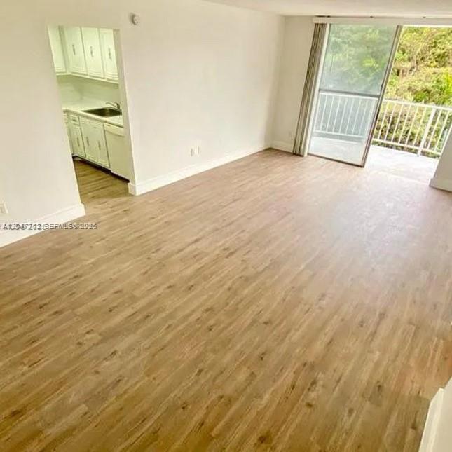 An open living area with light wood-look flooring leads to a kitchen and a balcony — 492 NW 165th St Rd # 415, Miami FL 33169, MIAMI, FL