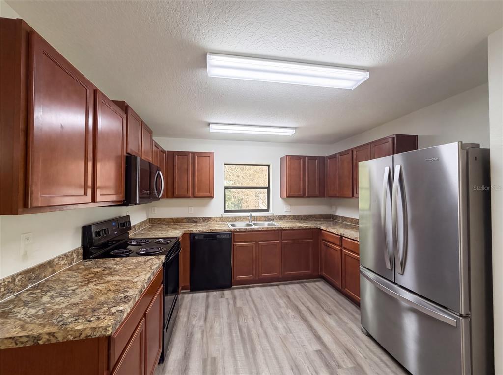A kitchen features wood cabinets, laminate countertops, stainless steel appliances, and light wood-look flooring — 2440 BRACKNELL FOREST TRAIL, TAVARES, FL