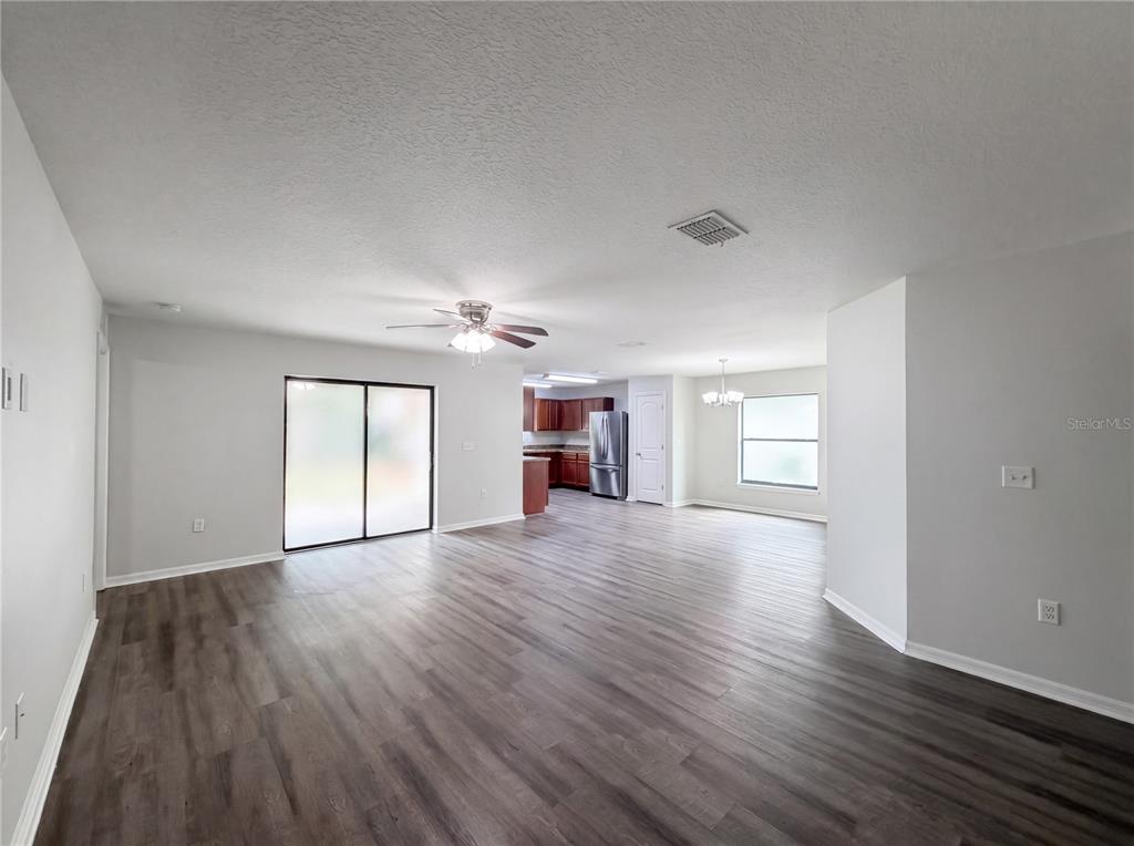 A spacious open-concept living and dining area features wood-look flooring and a kitchen with cabinets — 2440 BRACKNELL FOREST TRAIL, TAVARES, FL