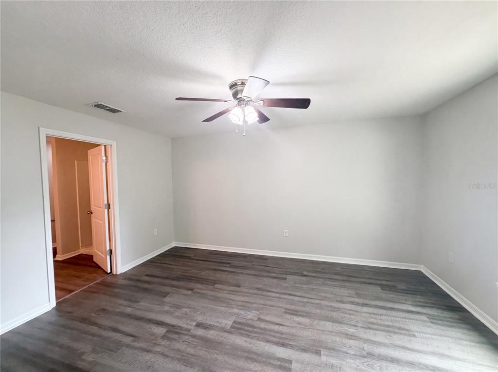 An empty bedroom features light gray walls, dark wood-look flooring, and a ceiling fan — 2440 BRACKNELL FOREST TRAIL, TAVARES, FL