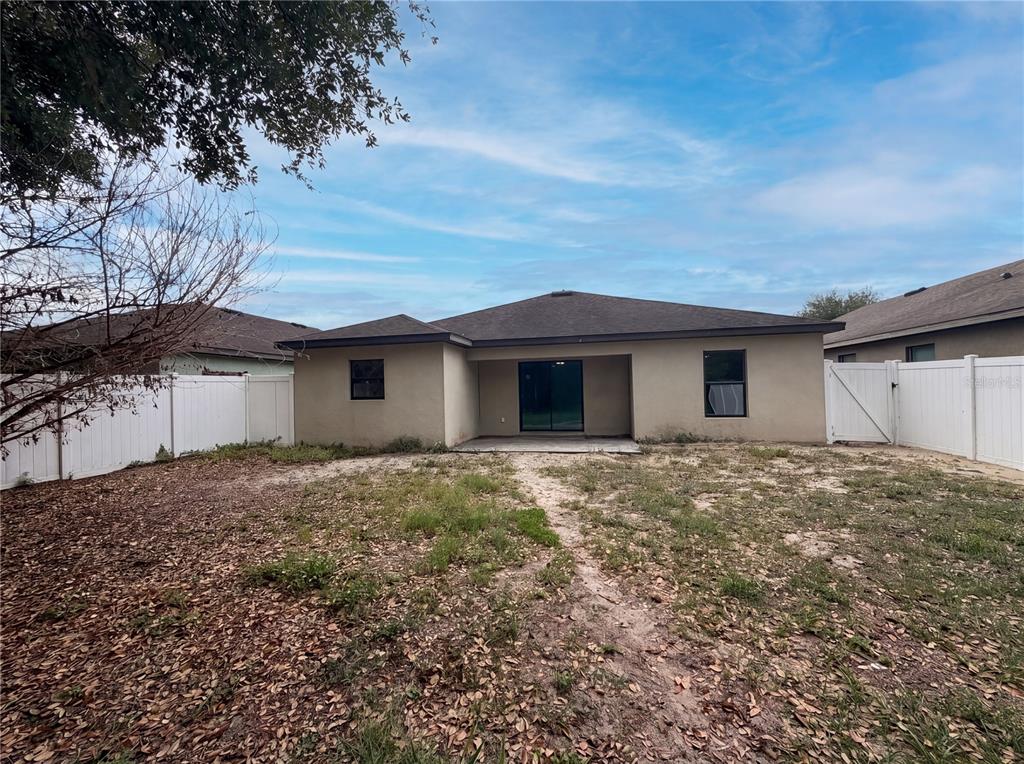 The exterior rear view of a single-story house features a concrete patio and fenced yard — 2440 BRACKNELL FOREST TRAIL, TAVARES, FL