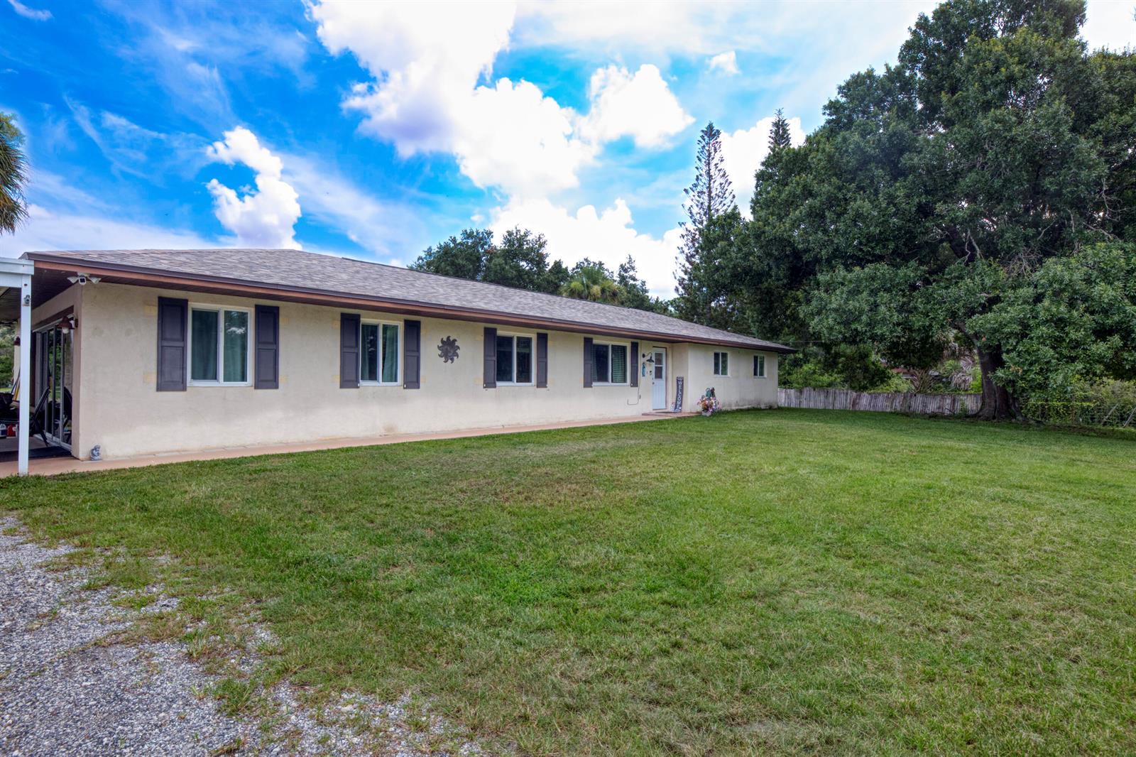 A single-story house with a beige stucco exterior, dark shutters, and a large grassy yard — 9302 Orange Avenue, Fort Pierce FL 34945, FORT PIERCE, FL