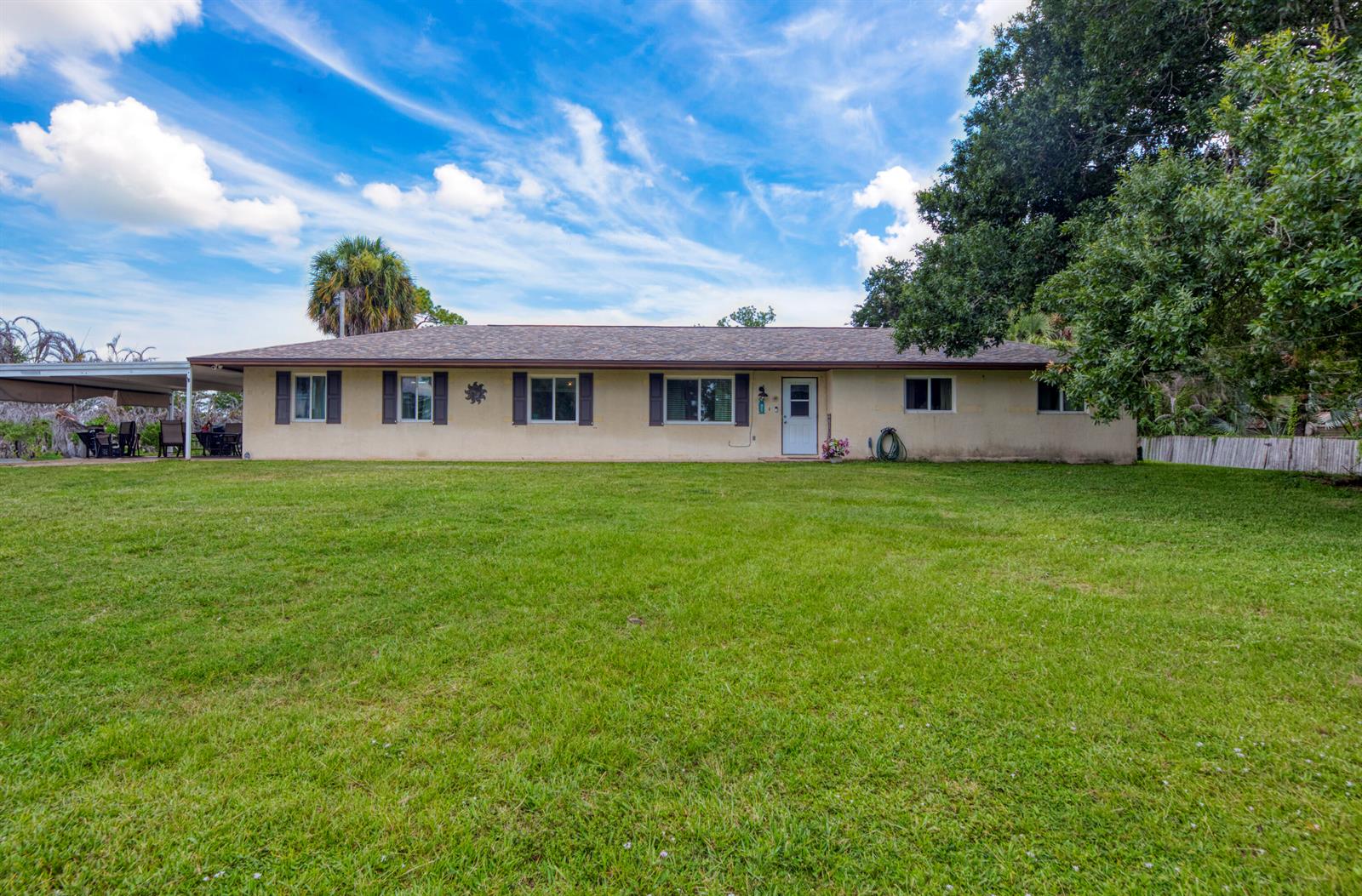 A single-story house with a beige exterior, dark shutters, and a large front lawn — 9302 Orange Avenue, Fort Pierce FL 34945, FORT PIERCE, FL