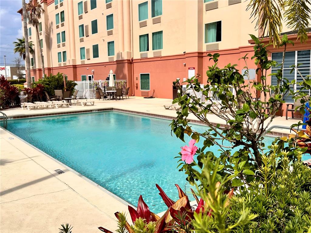 An outdoor swimming pool sits in front of a multi-story hotel building with landscaping — 3000 MAINGATE LANE UNIT 415, KISSIMMEE, FL
