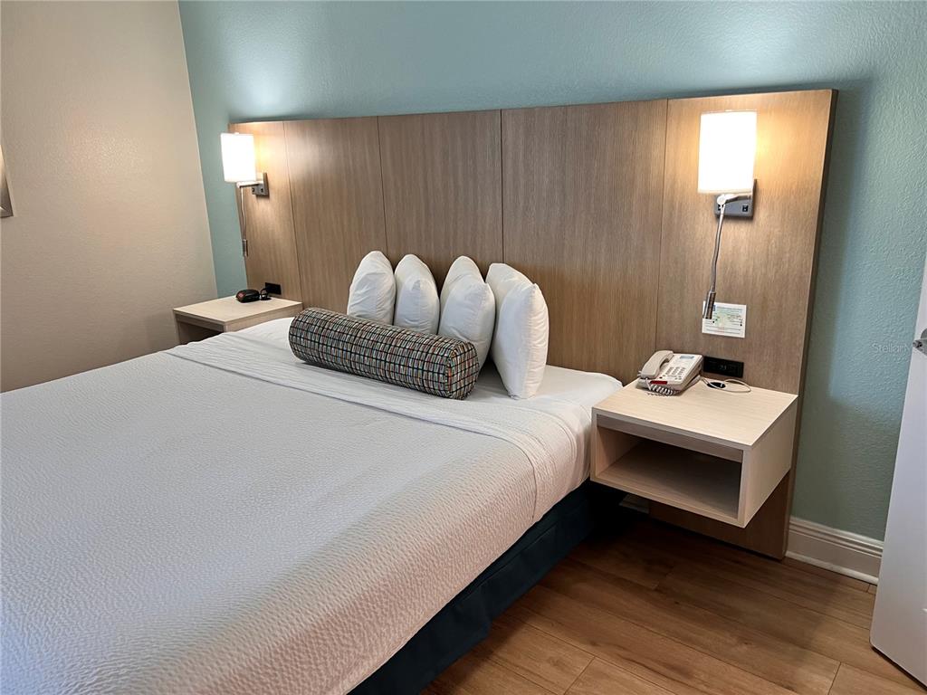 A hotel room features a bed with a wooden headboard, wall-mounted lamps, and nightstands — 3000 MAINGATE LANE UNIT 415, KISSIMMEE, FL