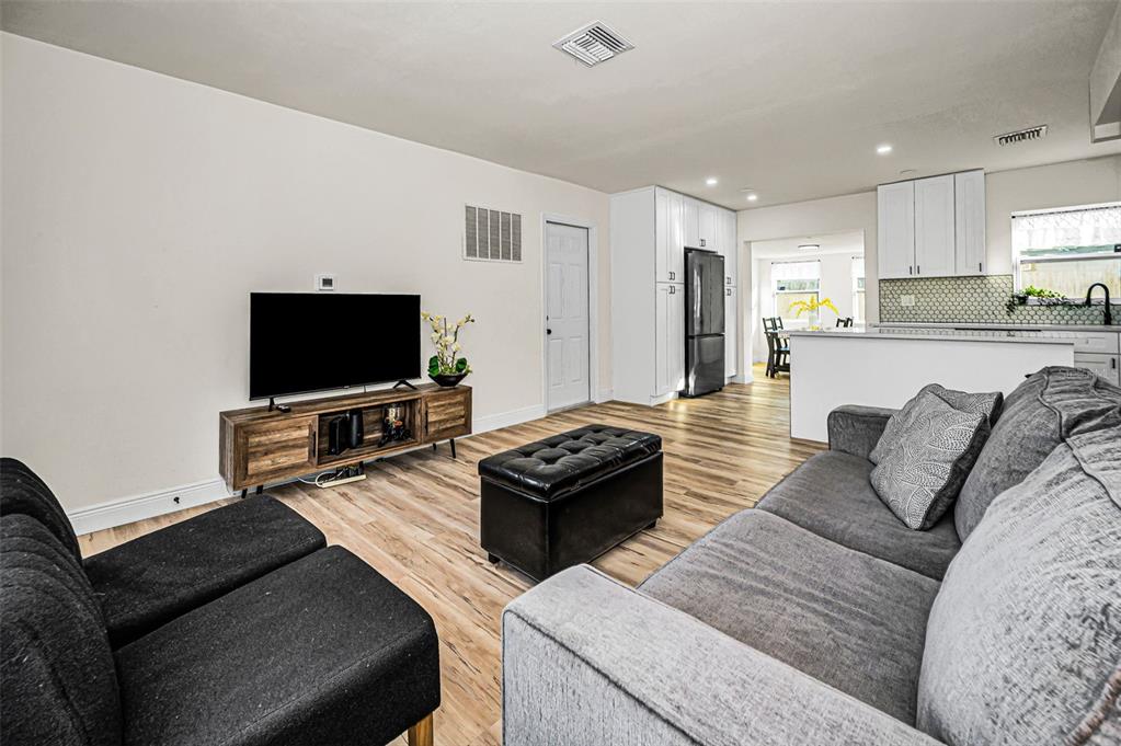 A living room with light wood-look flooring, a grey sofa, and an open-concept kitchen — 1231 LITTLE JOHN LANE, DUNEDIN, FL