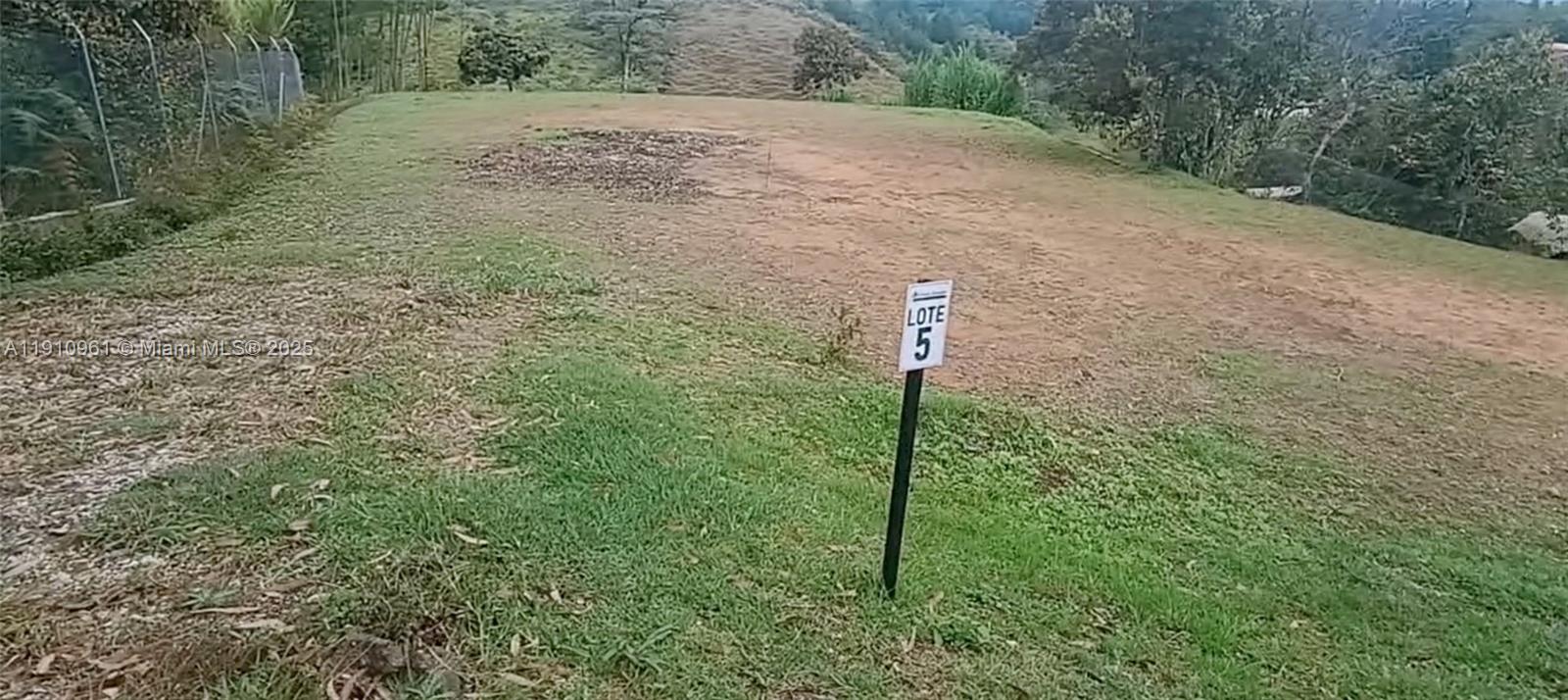 A sign labeled Lote 5 stands on a grassy, sloped plot of land — Vereda Mmpuesto Sector Garrido #5, C Colombia, C