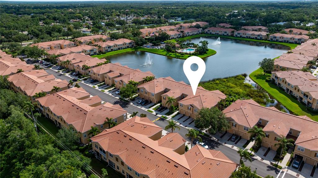 An aerial view shows a residential complex with tile roofs surrounding a central lake — 3760 PARKRIDGE CIRCLE UNIT 23-204, SARASOTA, FL