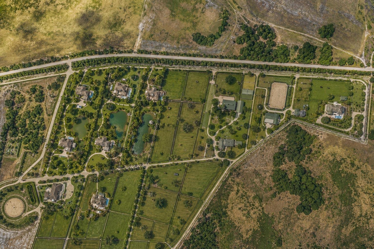 Aerial view of a rural estate featuring multiple houses, green pastures, ponds, and riding arenas — 0000 Hill Grade Road, Clewiston FL 33440, CLEWISTON, FL