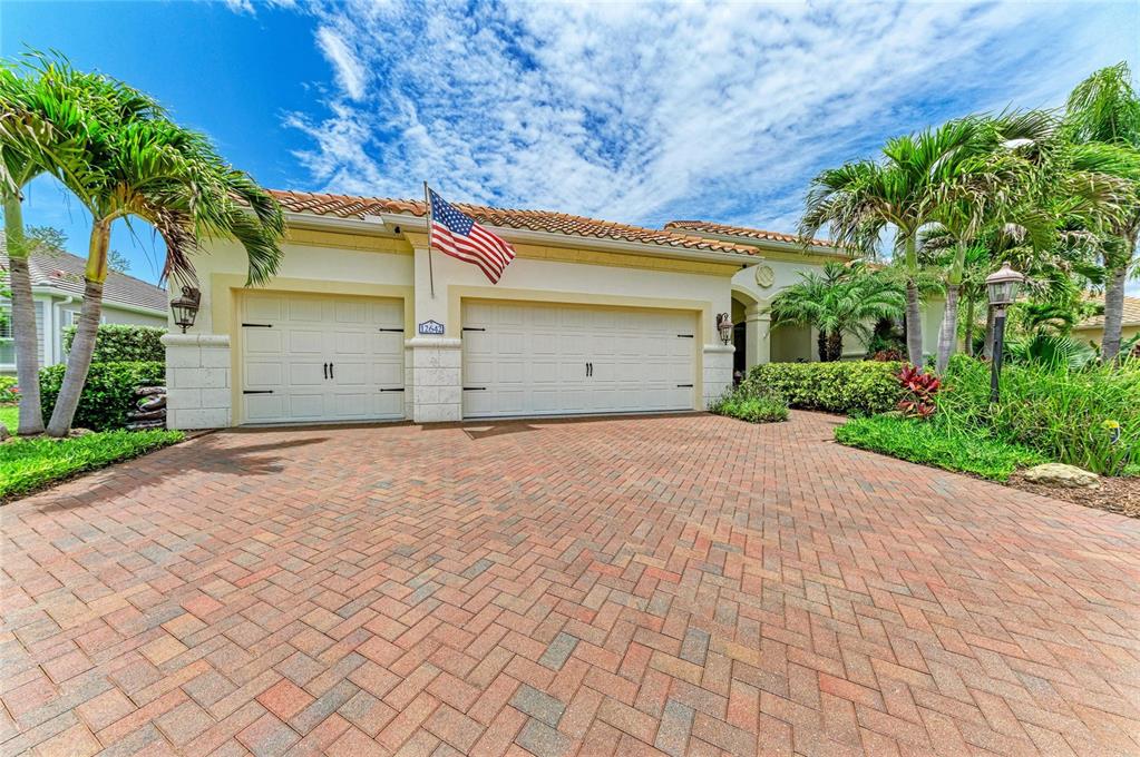 A house exterior features a brick paver driveway, two garage doors, and an American flag — 12642 HARNEY STREET, VENICE, FL