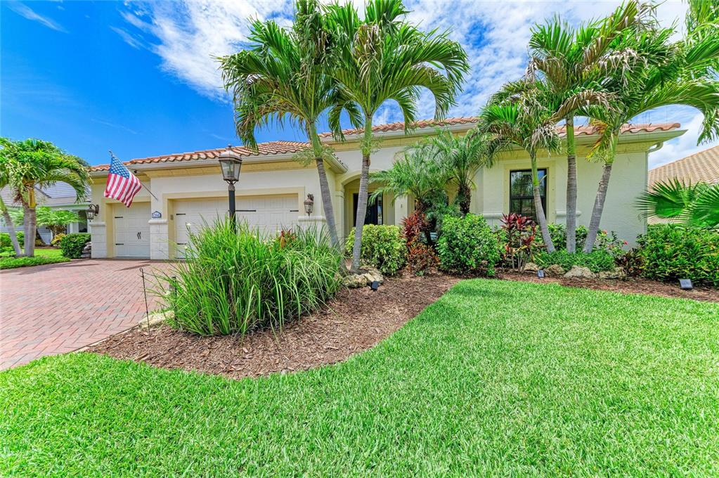 A single-story house with a brick paver driveway, palm trees, and a manicured lawn — 12642 HARNEY STREET, VENICE, FL