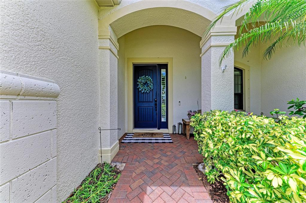 A front entryway features a dark blue door, brick pavers, and a lush green hedge — 12642 HARNEY STREET, VENICE, FL