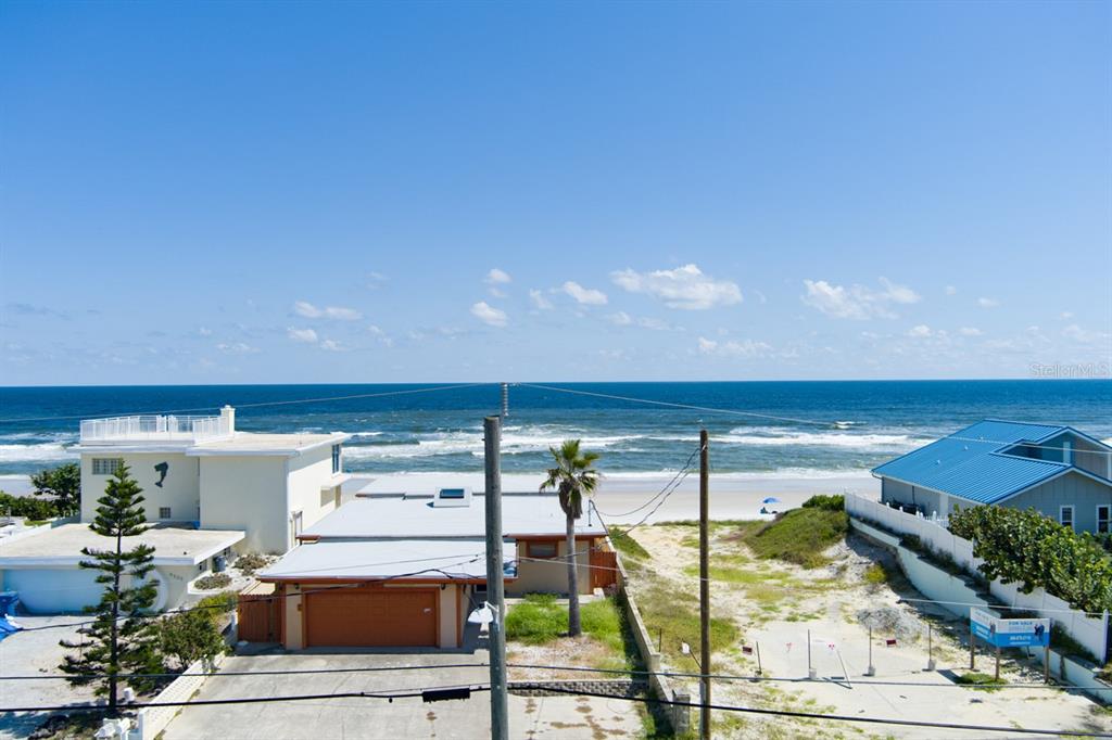 An elevated view of a beach house with a garage, palm tree, and oceanfront scenery — 4207 S ATLANTIC AVENUE, PORT ORANGE, FL