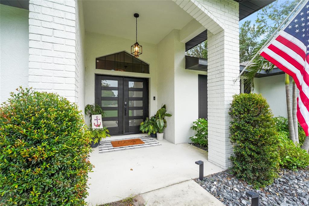 A white brick house exterior features a double front door, a porch, and an American flag — 13622 11TH TERRACE E, BRADENTON, FL