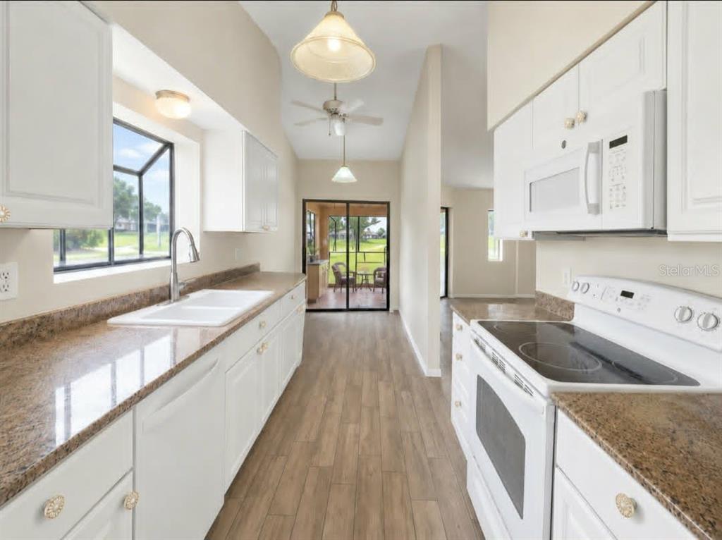 A galley kitchen features white cabinets, granite countertops, a white stove, and wood-look flooring — 1203 SAXONY CIRCLE UNIT A, PUNTA GORDA, FL