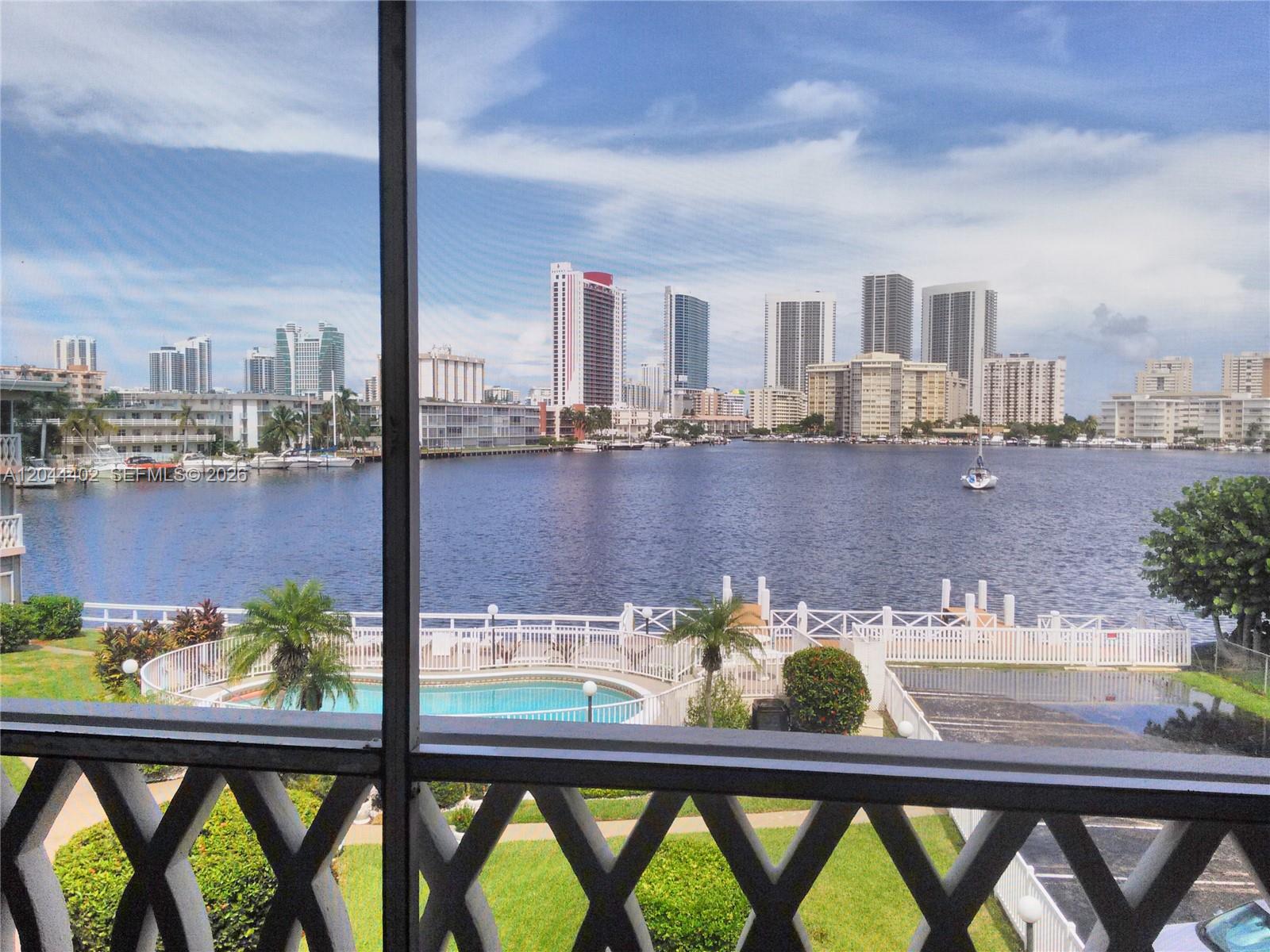 A view of a waterfront pool and city skyline seen through a screened balcony — 450 GOLDEN ISLES DR # 2H, Hallandale Beach FL 33009, HALLANDALE BEACH, FL