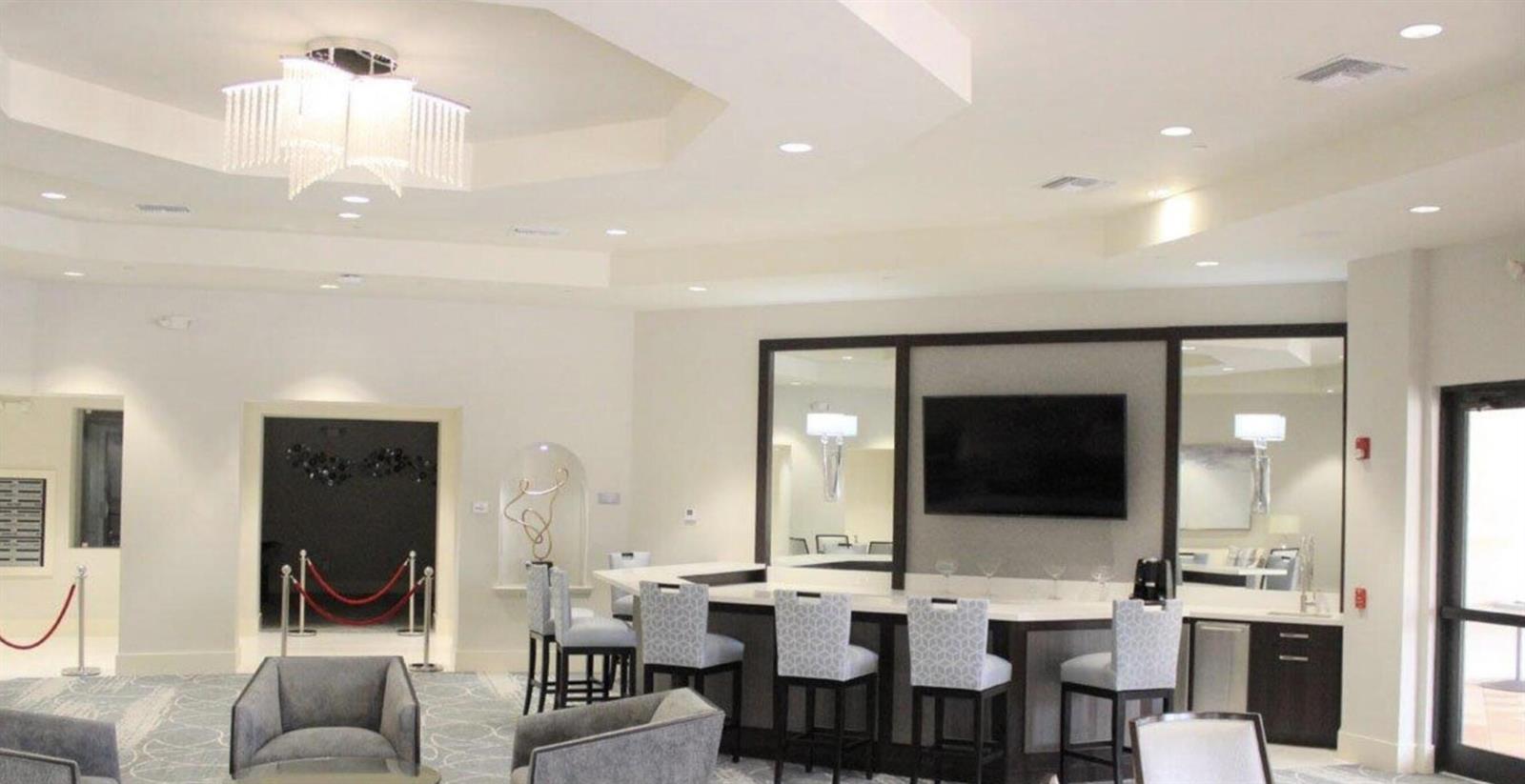 A modern lounge area features a bar with stools, a television, and a crystal chandelier — , West Palm Beach FL 33411, WEST PALM BEACH, FL