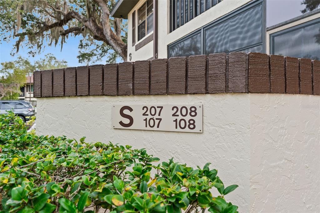 A sign on a stucco wall indicates building S contains units 107, 108, 207, and 208 — 19505 QUESADA AVENUE UNIT S208, PORT CHARLOTTE, FL