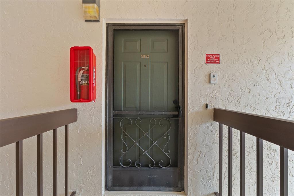 An exterior view of a residential unit entrance with a screen door and fire extinguisher — 19505 QUESADA AVENUE UNIT S208, PORT CHARLOTTE, FL