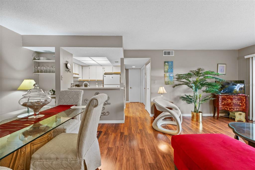 A living and dining area with wood-look flooring, a glass table, and an open kitchen — 19505 QUESADA AVENUE UNIT S208, PORT CHARLOTTE, FL