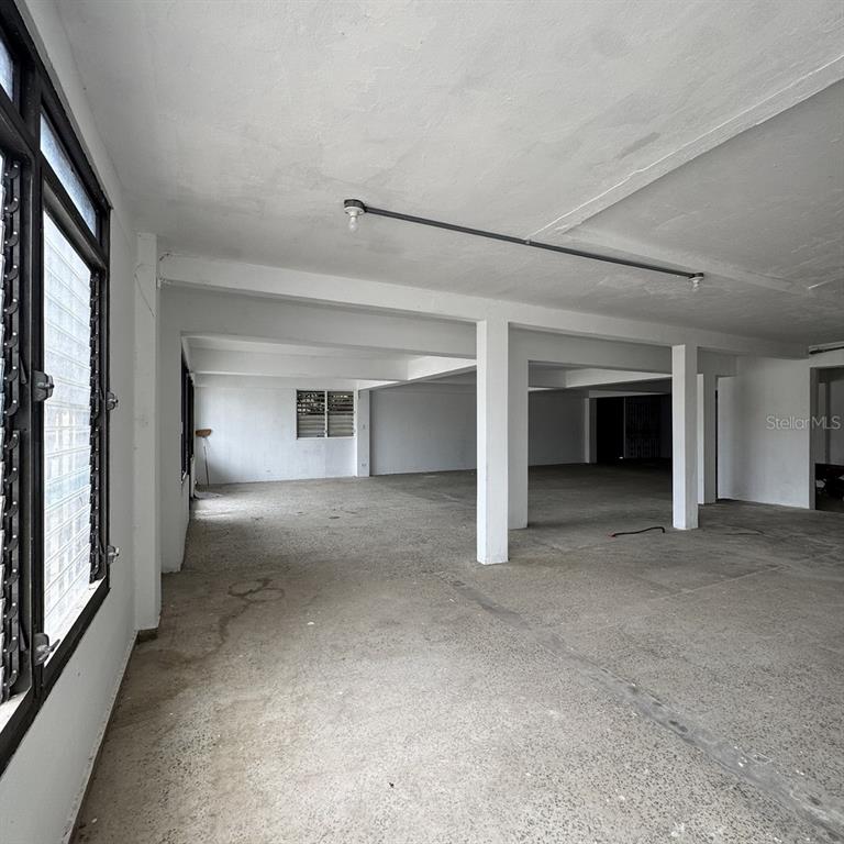 An open, unfinished interior space with concrete floors, white support columns, and jalousie windows — Calle 3 URB. FLAMBOYAN UNIT A-3, MANATI, PR